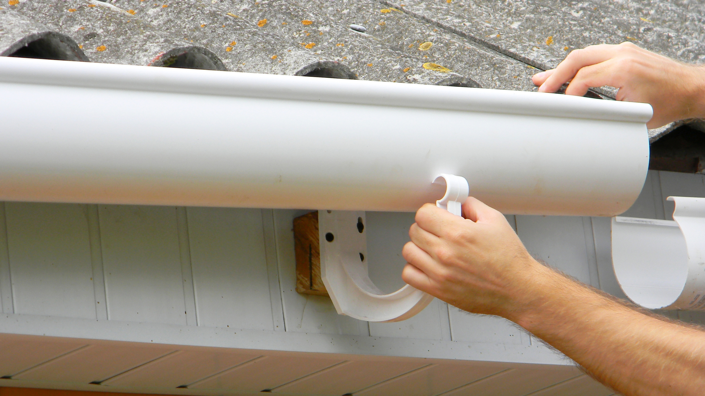 A person installing or adjusting a white gutter on a building.