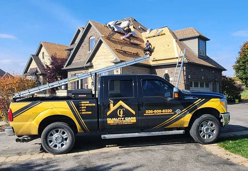 A roofing crew replacing shingles on a residential house with a truck parked in the driveway.