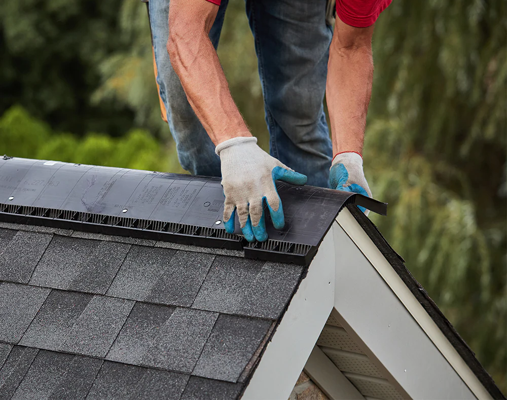 A worker installing or repairing asphalt roofing shingles on a house roof, using a strip of underlayment membrane.