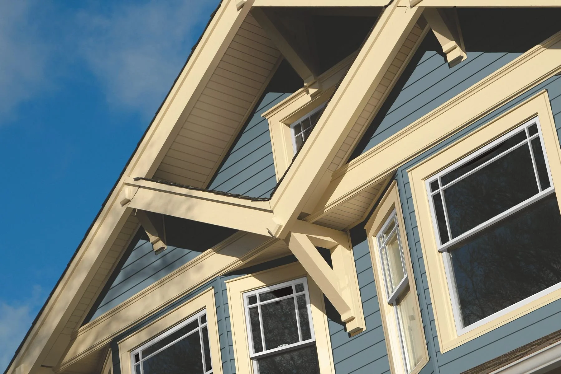 Close-up of the upper part of a blue house with white trim, showing windows and architectural details against a blue sky.