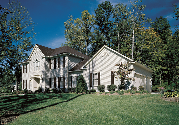Large white two-story house with dark roof, surrounded by a well-maintained lawn and trees.