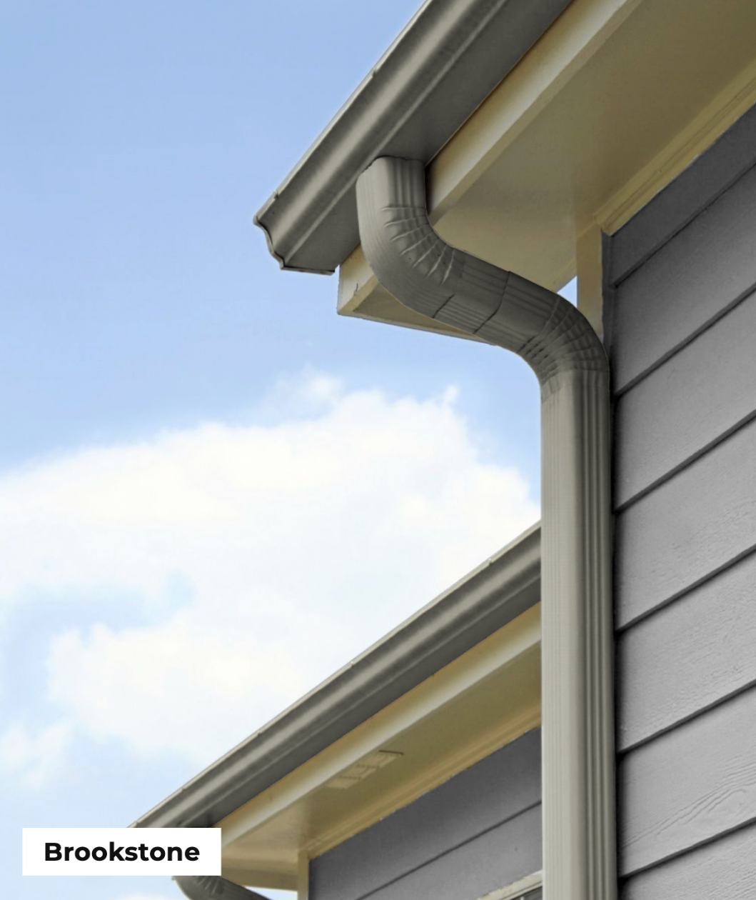 Close-up of a house's exterior corner showing gray siding, beige trim, and a metal gutter system against a blue sky with clouds.