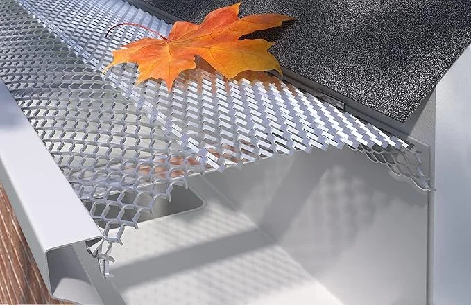 Close-up of outdoor furniture with a metal grid surface, a colorful autumn maple leaf, and a dark textured tile area.