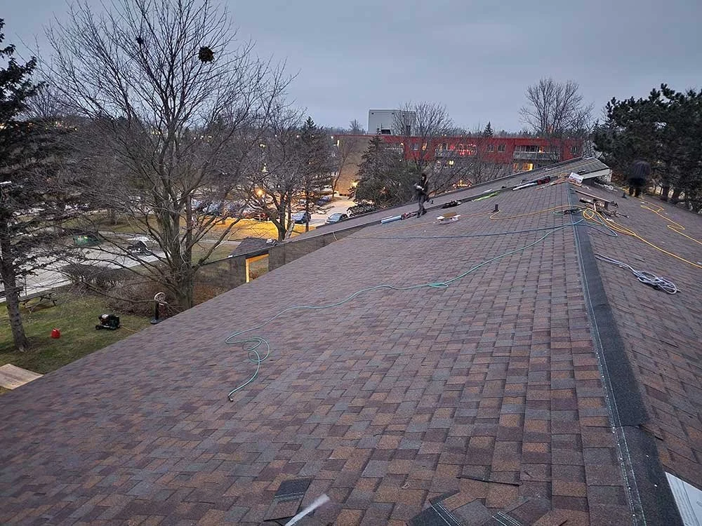 Workers installing solar panels on the roof of a building with trees and a parking lot in the background.