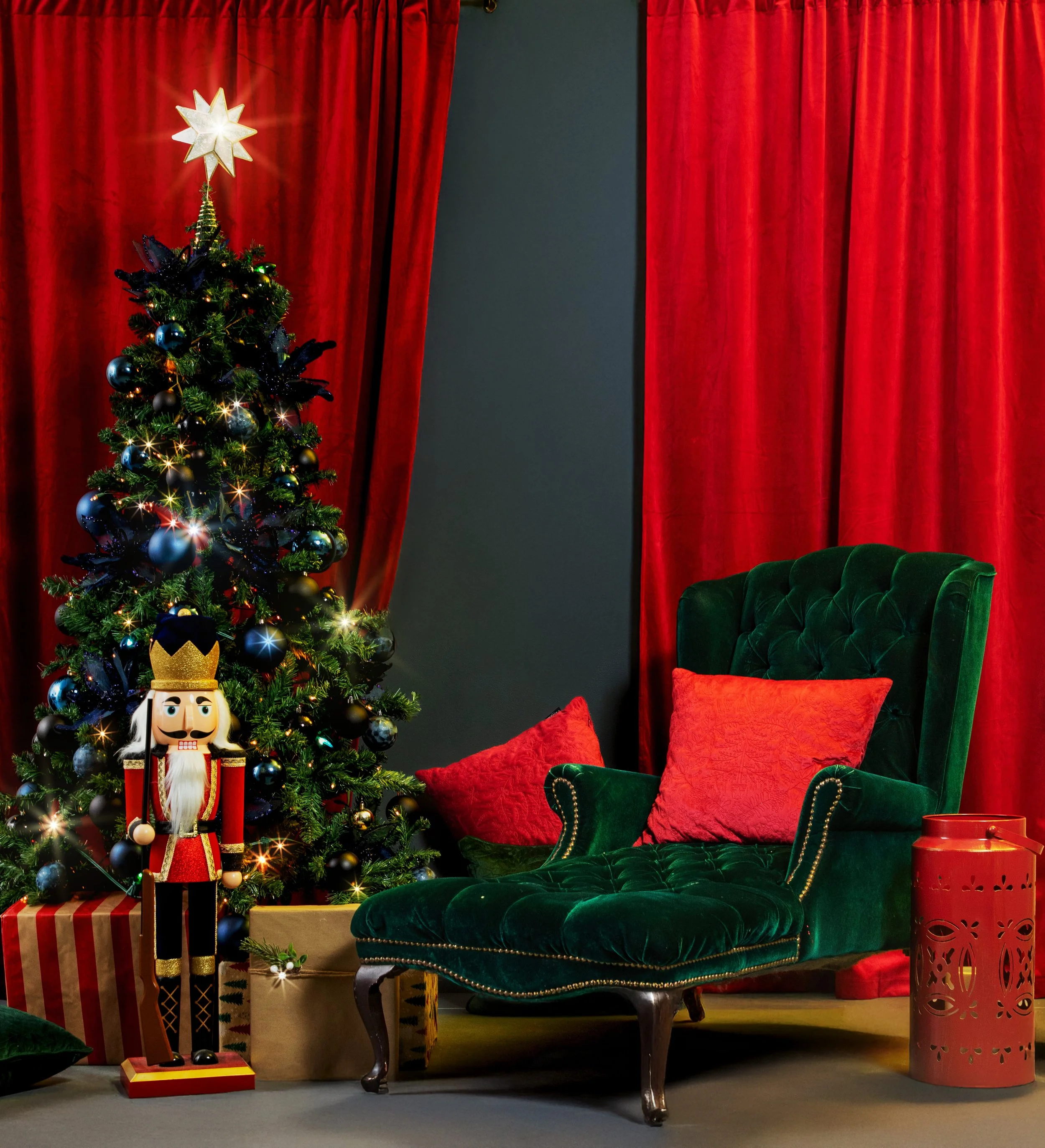 Salon de Noël avec sapin décoré, fauteuil vert en velours, coussins rouges, rideaux rouges, nutcracker en bois, et une lanterne rouge.