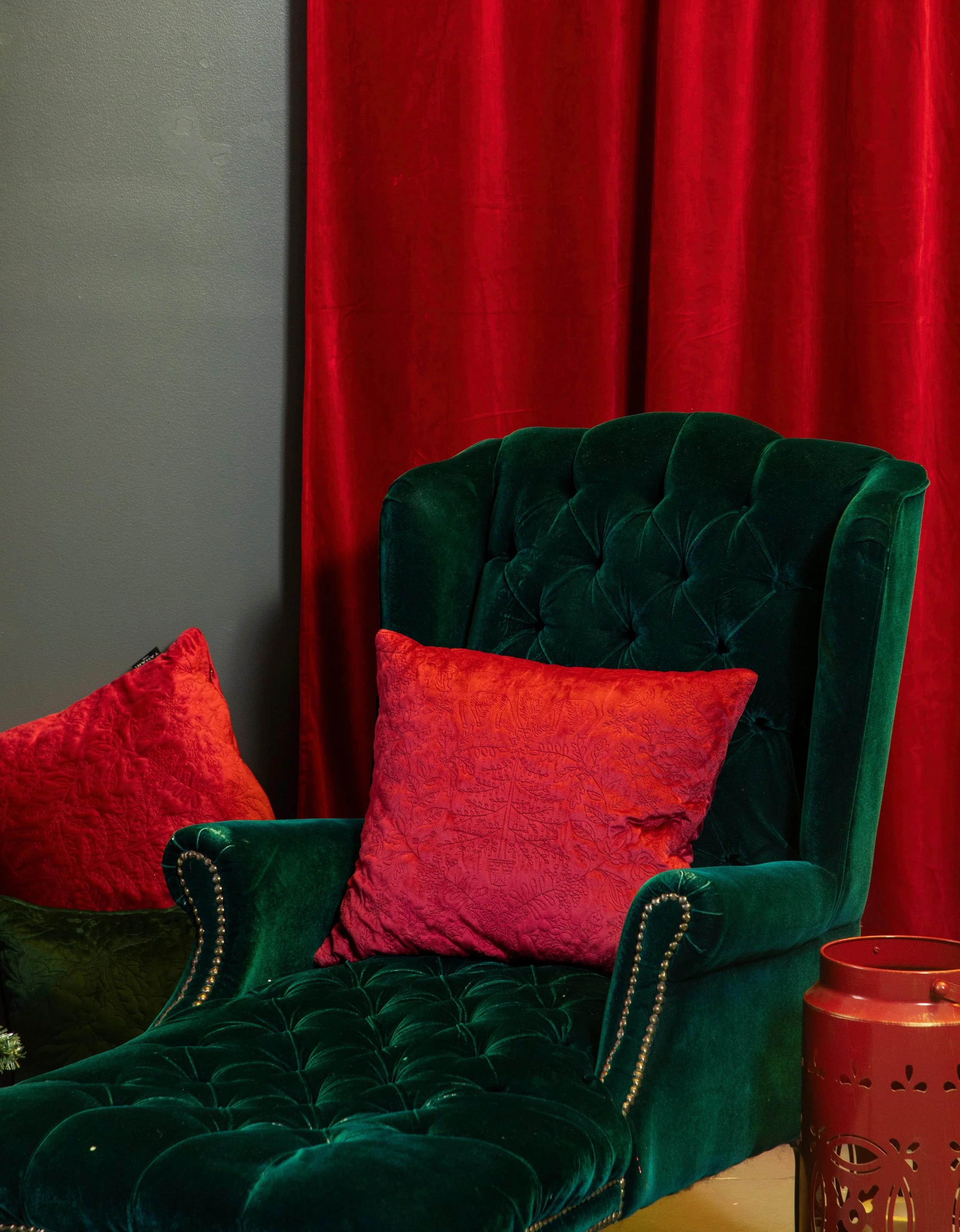 Un fauteuil vert en velours avec deux coussins rouges, devant un rideau rouge, dans une pièce décorée pour Noël.