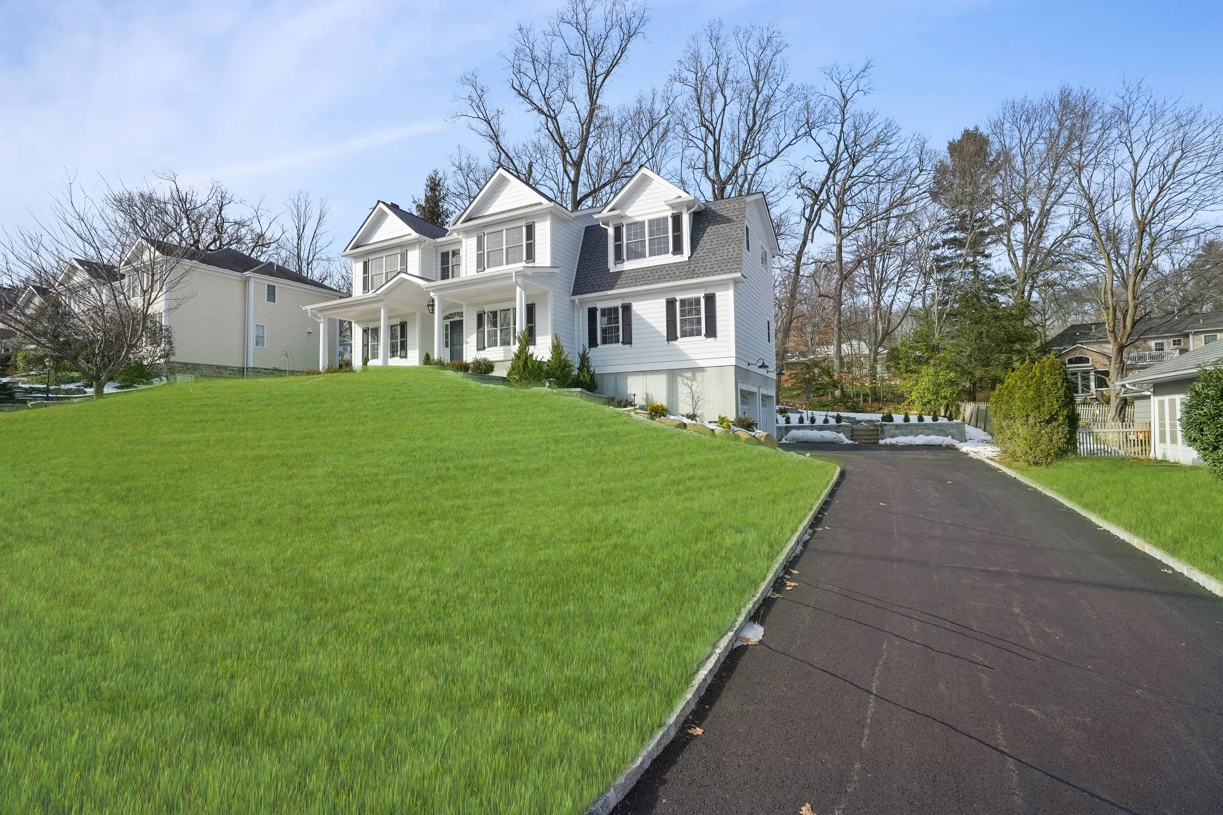 Front view of a white, two-story house with green lawn and a driveway on a sunny day.