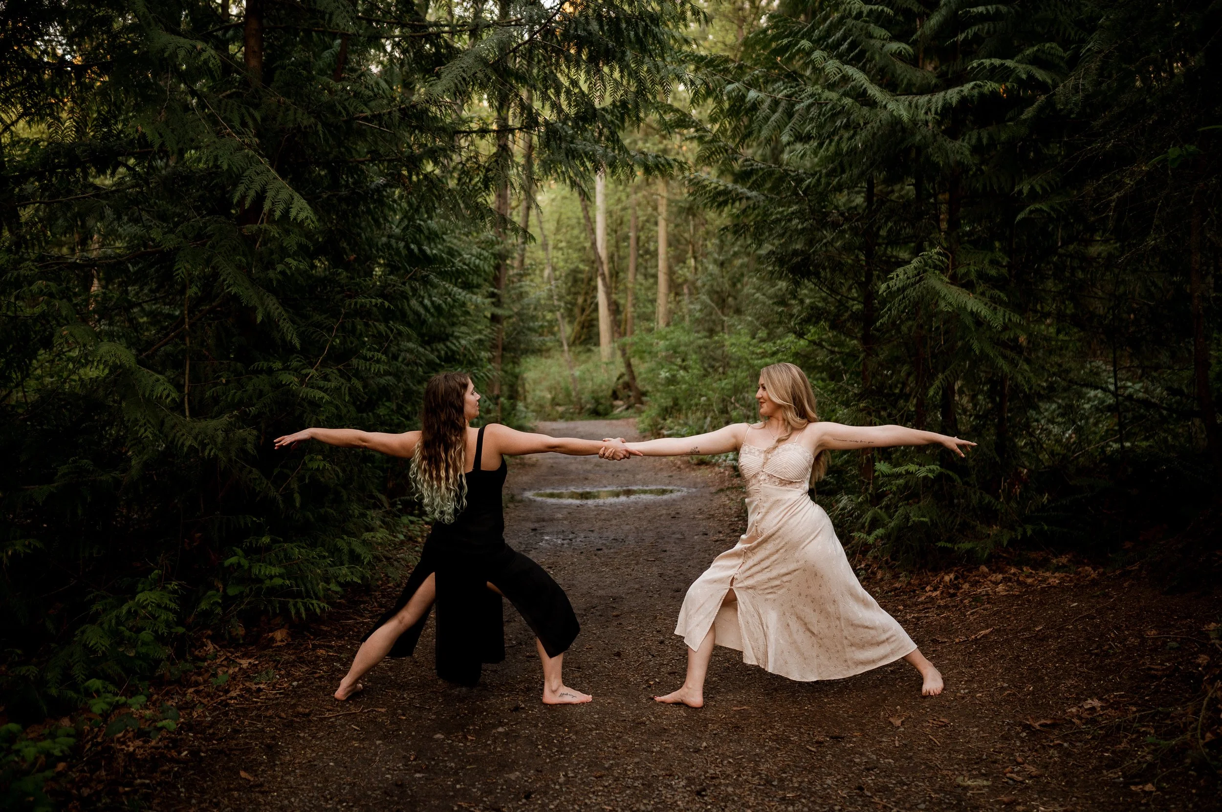 two women joining hands and posing in a forest