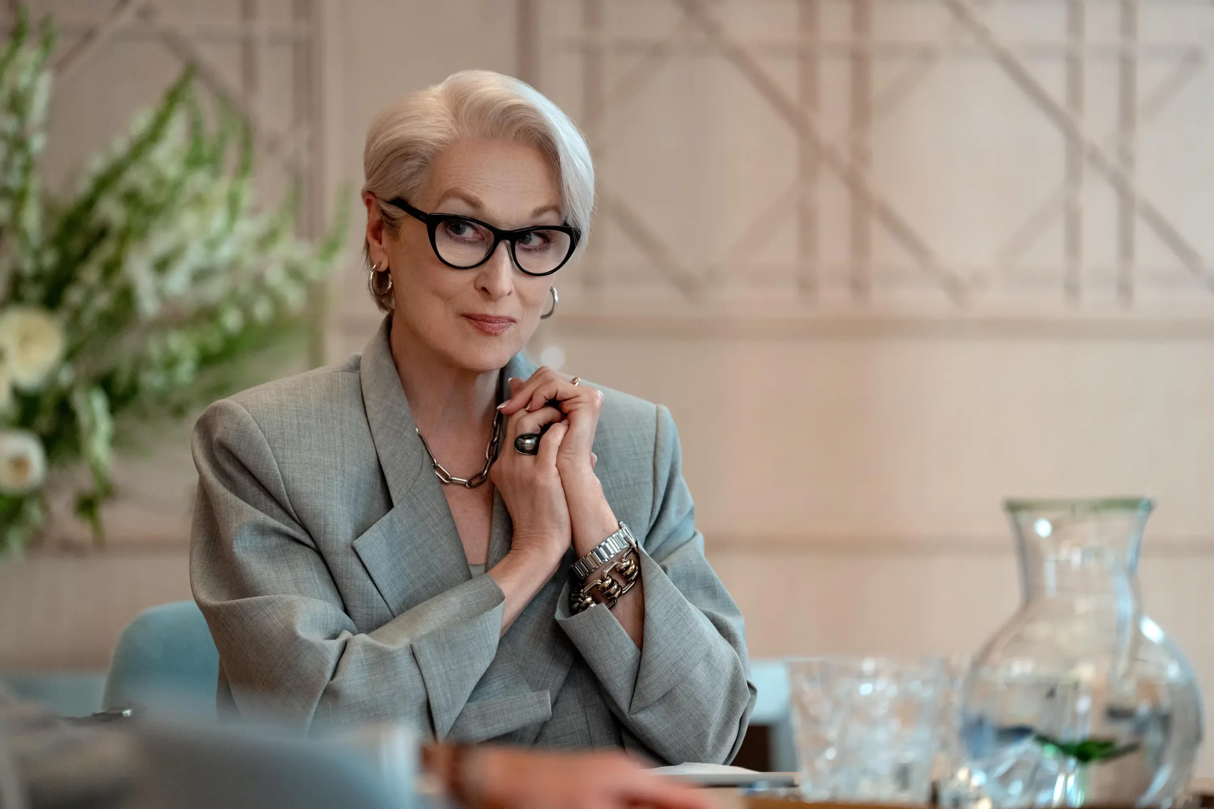 An image of Meryl Streep as Miranda Priestly in The Devil Wears Prada 2. Her hands are clasped in front of her, and she is looking past the camera, inquisitively towards someone (not pictured) 