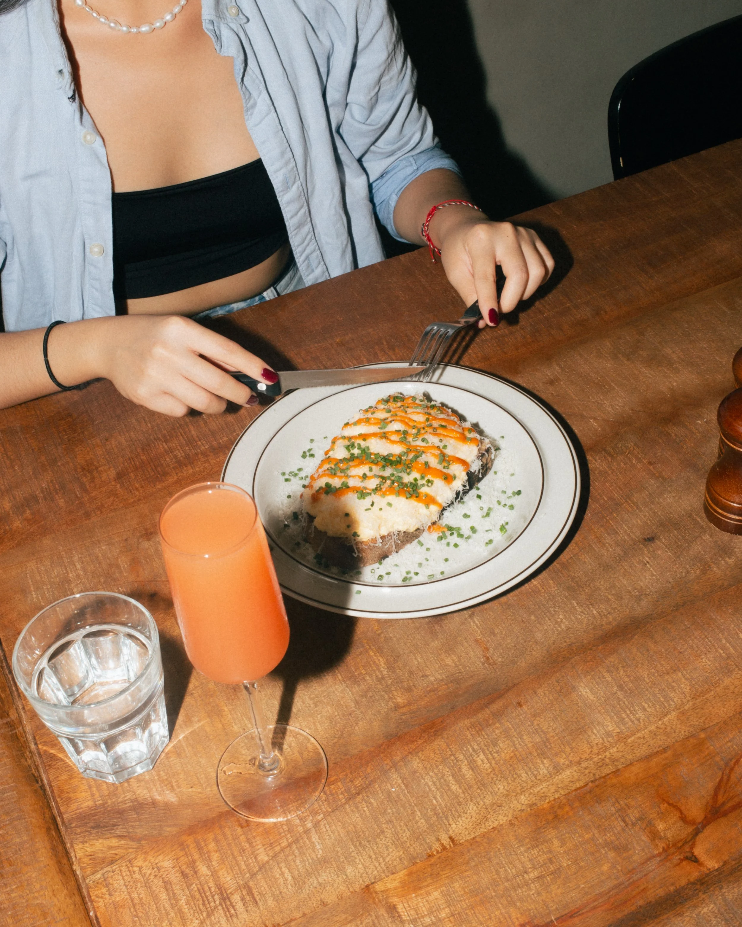 A person enjoying creamy scrambled eggs on toast with parmesan and chives, served with a fresh juice at Sirene Cafe, a specialty brunch spot in Berlin Prenzlauer Berg.