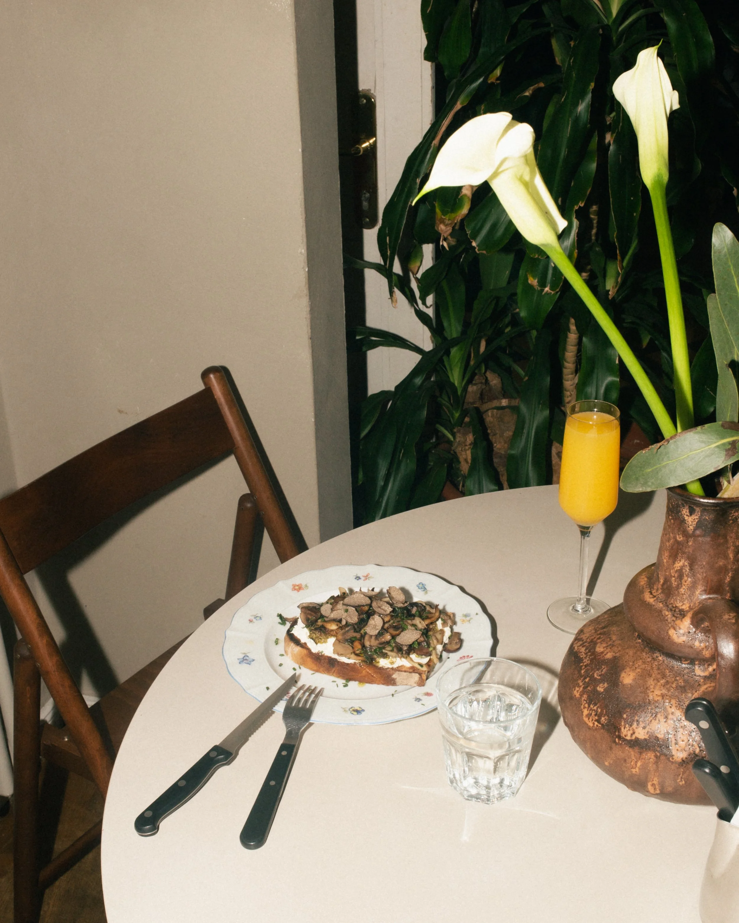 A delicious plate of sourdough toast topped with mushrooms and herbs, served with fresh orange juice on a rustic round table at a leafy Berlin brunch cafe.