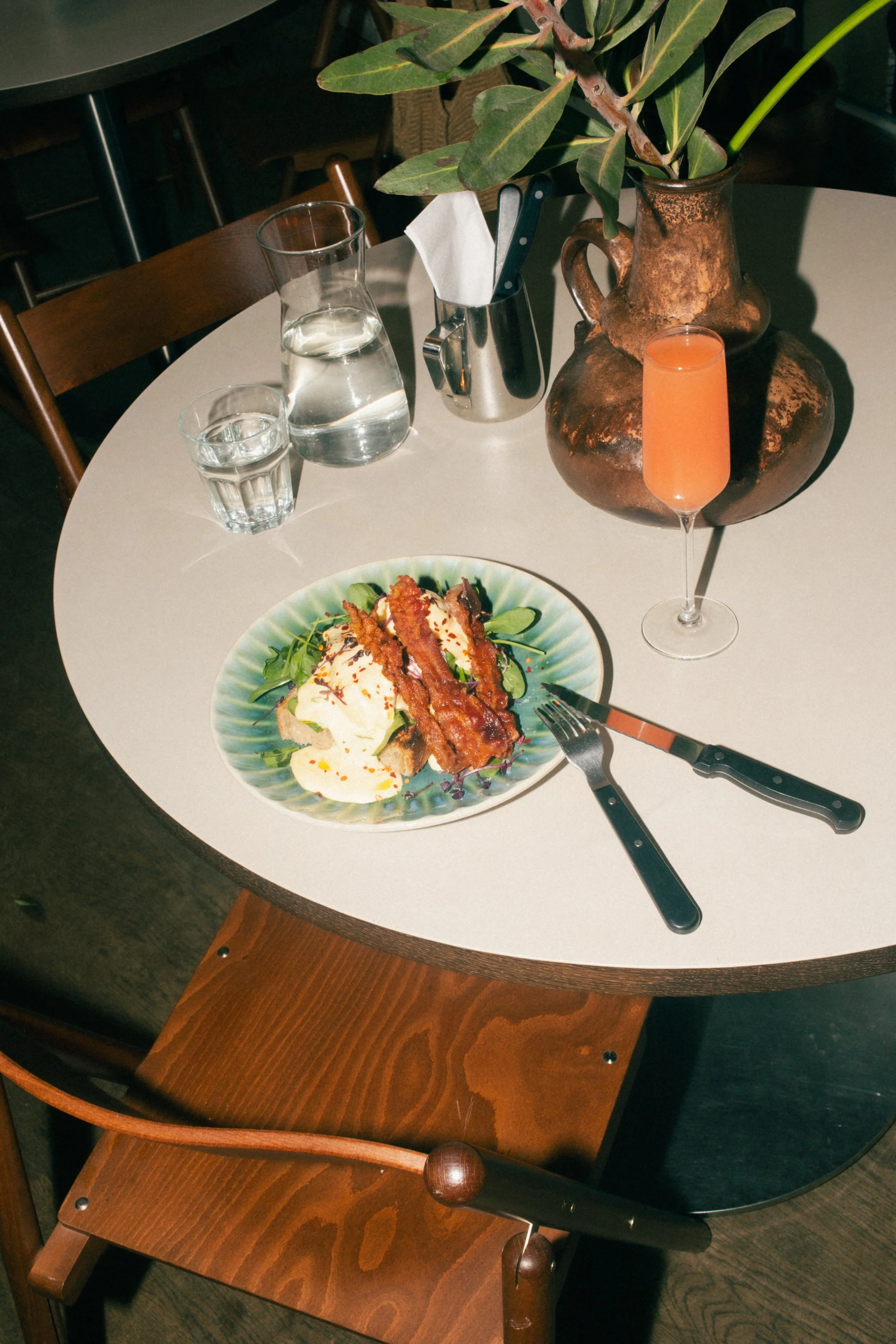 A delicious plate of Eggs Benedict served with a tall glass of fresh orange juice and sparkling water on a wooden table at a leafy Berlin brunch cafe.