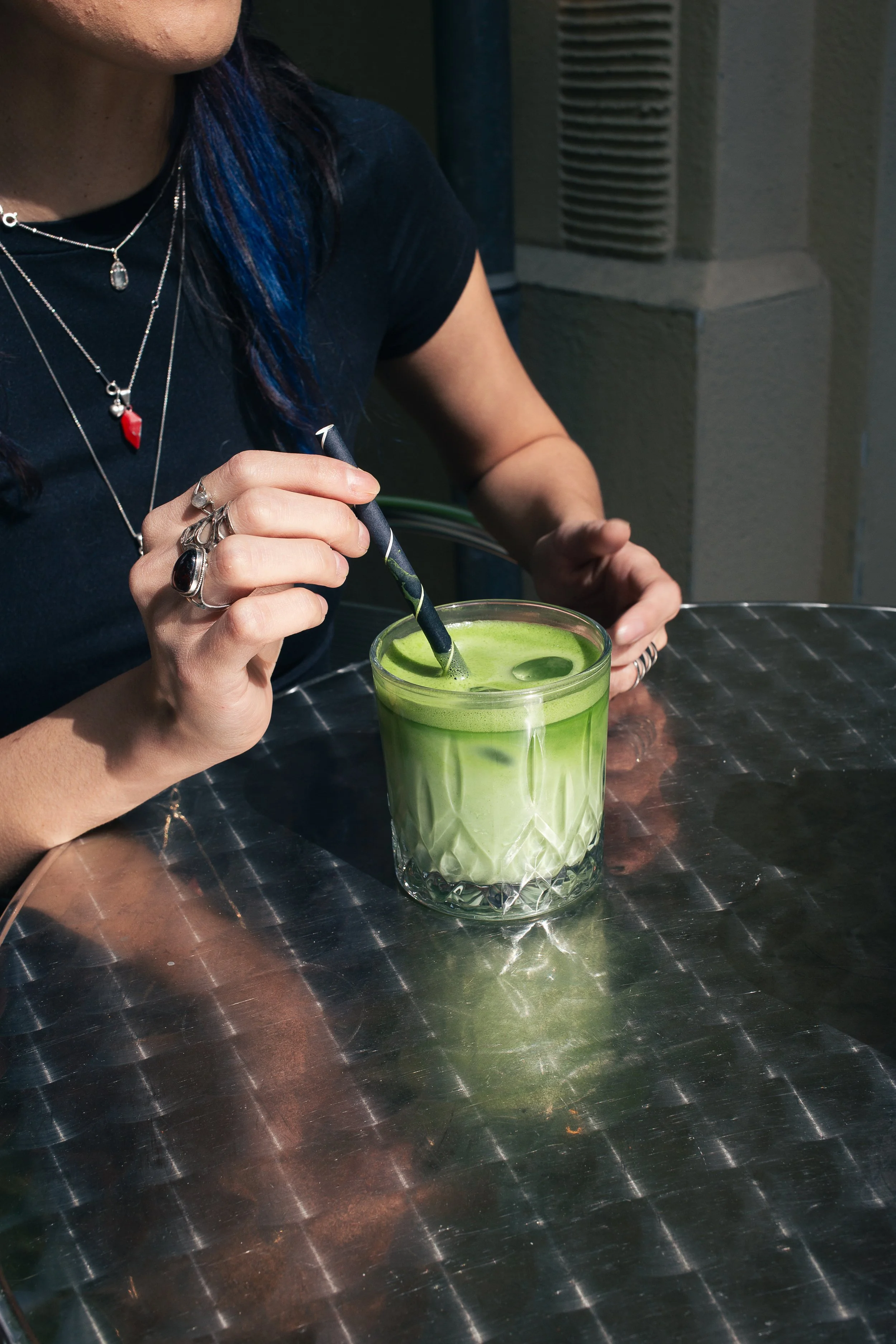 A person with rings stirring a ceremonial matcha latte with a striped straw at a specialty cafe in Berlin, Mitte.