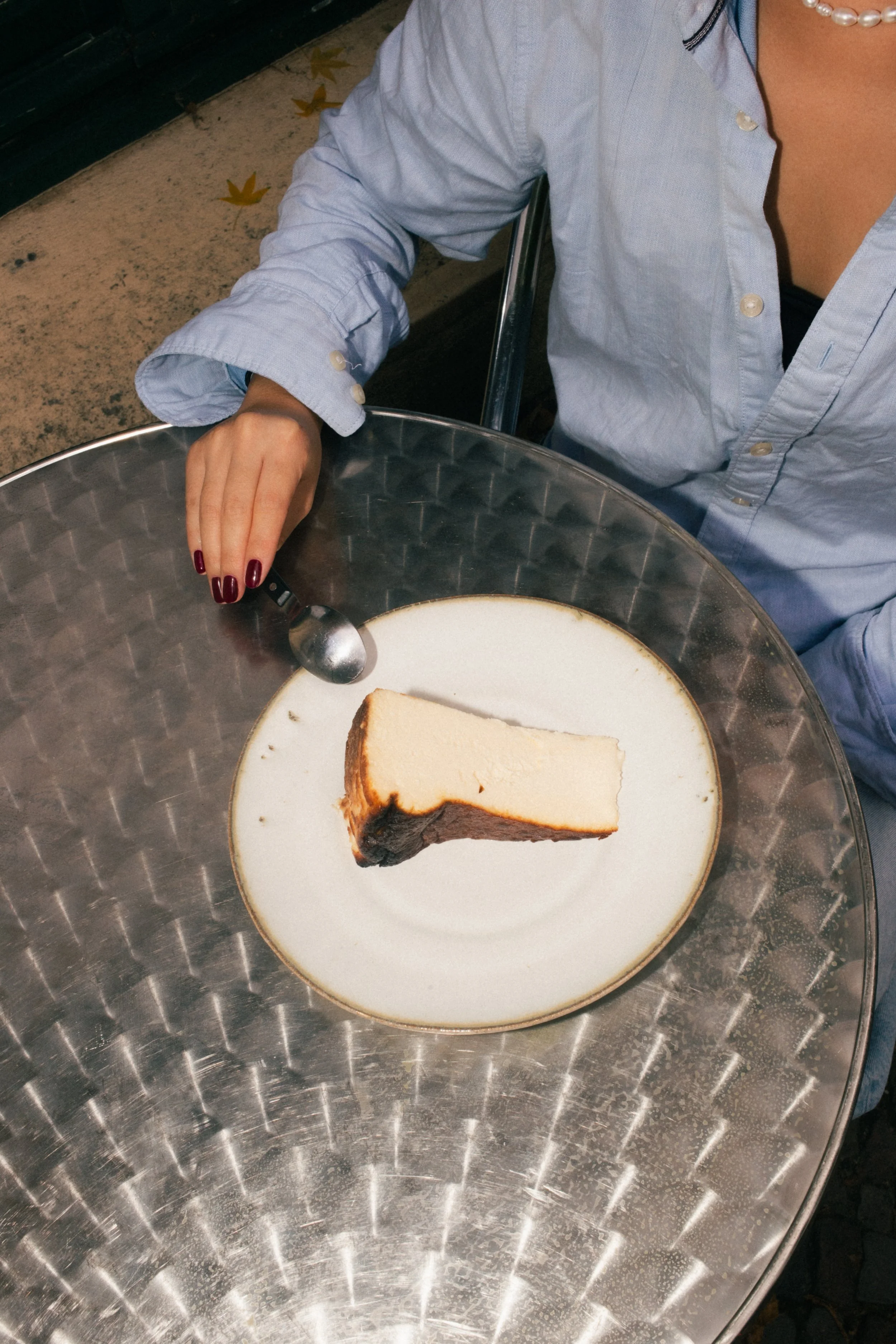 Close-up of a Basque cheesecake slice on a round wooden table, held by a person with a silver spoon in a trendy Berlin, Prenzlauer Berg brunch spot.