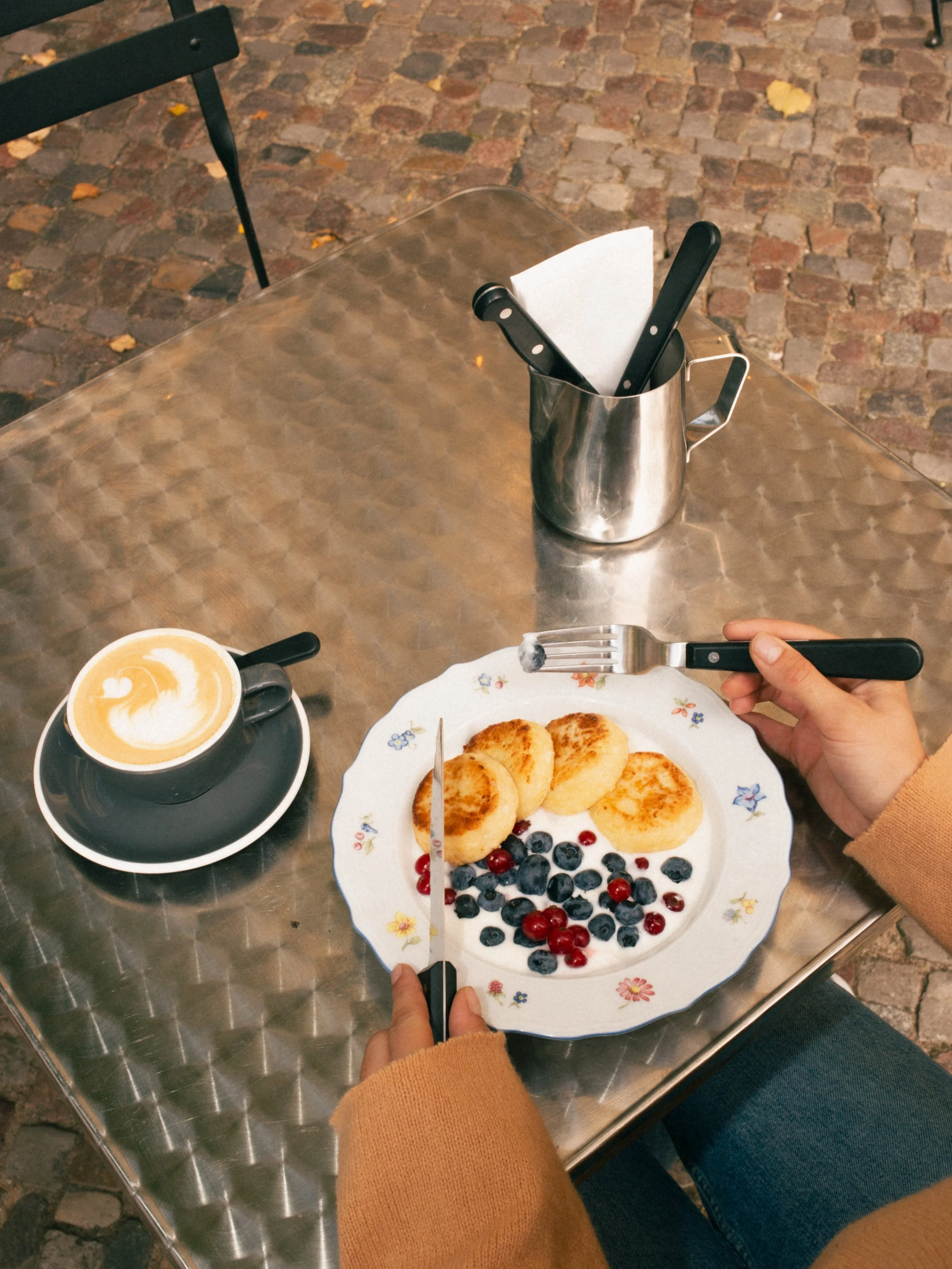 Golden fried syrniki (cottage cheese pancakes) served with sour cream and seasonal berries on a ceramic plate at a specialty brunch cafe in Berlin.