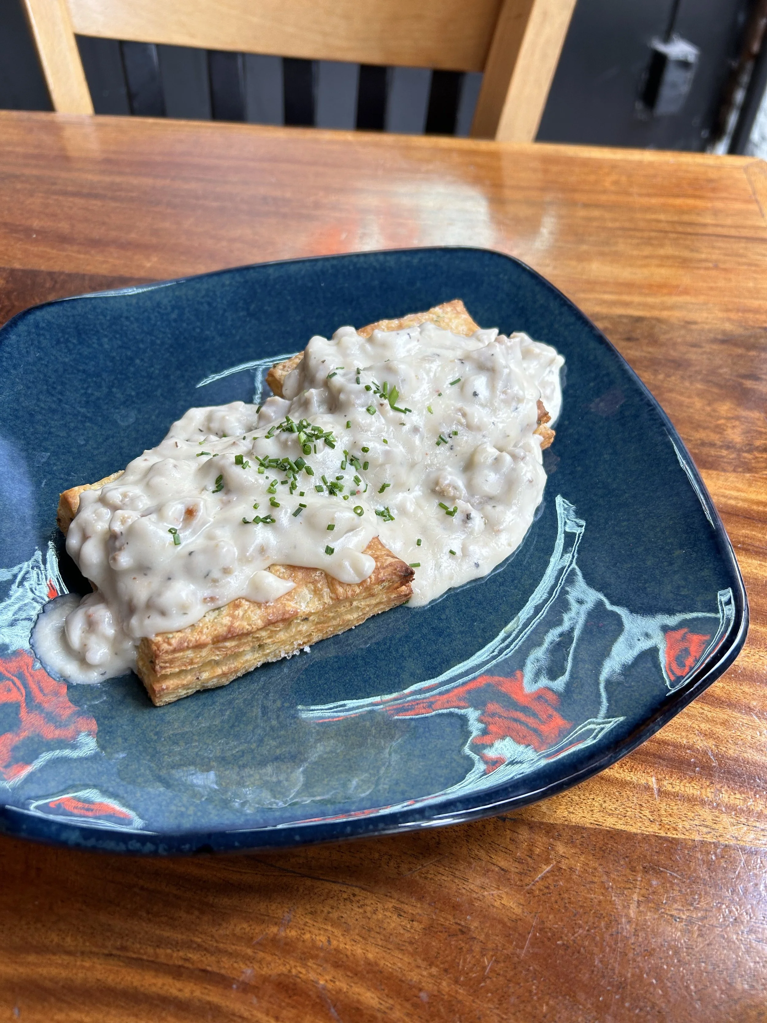 A serving of beef stew pie topped with creamy gravy and garnished with chopped chives on a blue plate, placed on a wooden table.