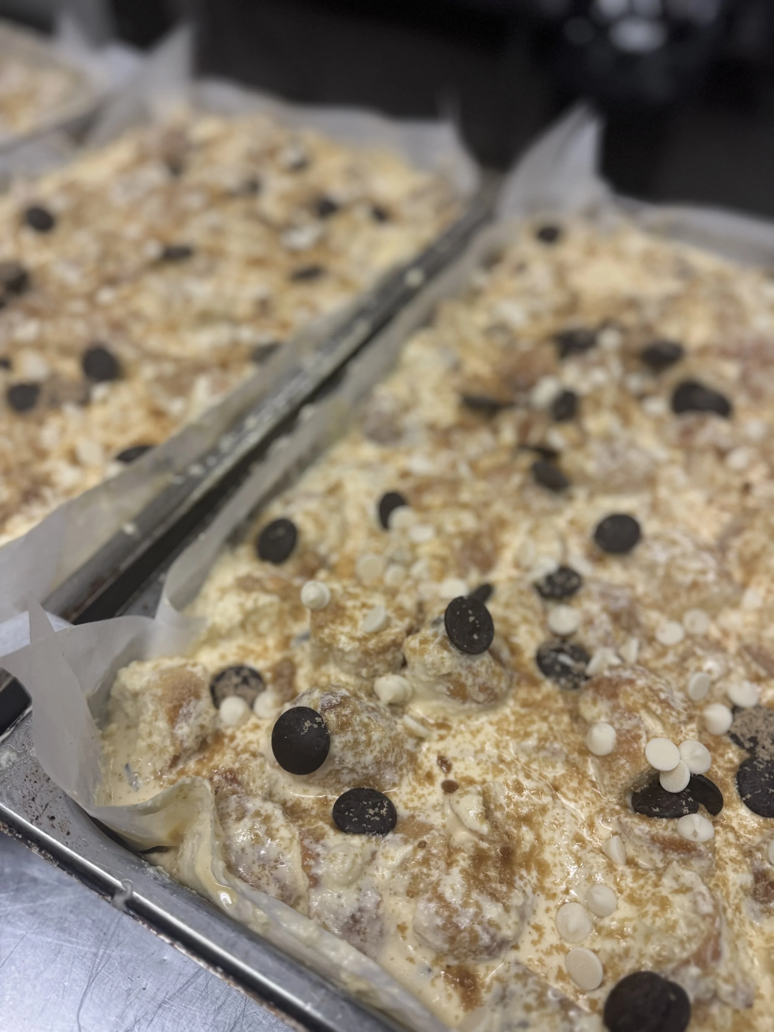 Two trays of unbaked cake or pastry topped with chocolate chips and white chocolate chips.