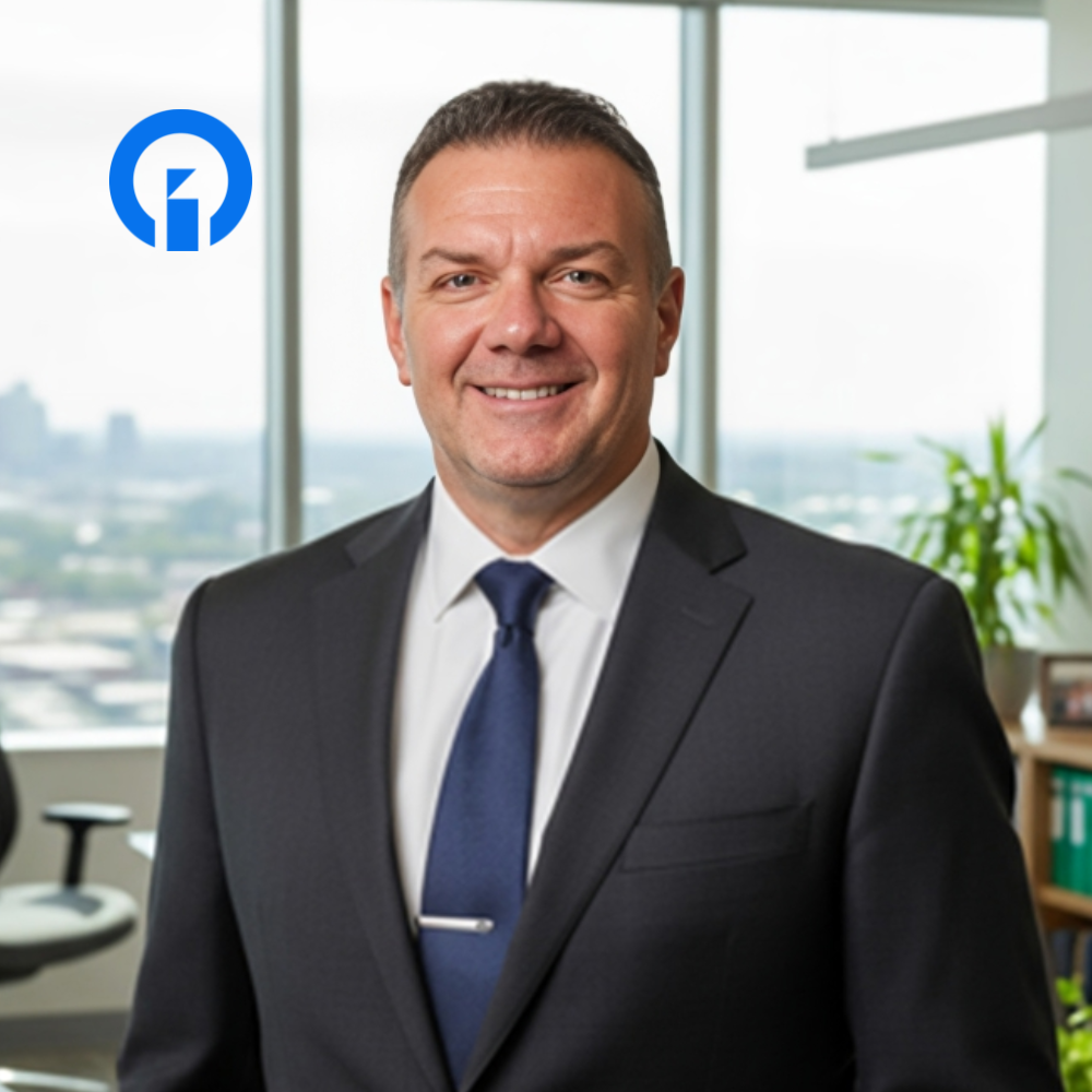 Professional man in a suit smiling in an office with a city view, with a blue logo in the background.