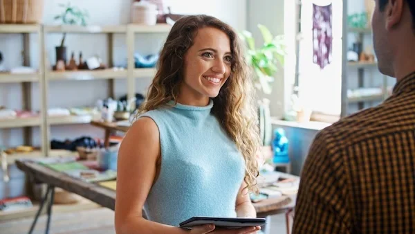 A woman smiling and holding a tablet while talking to a man in an arts and crafts studio.