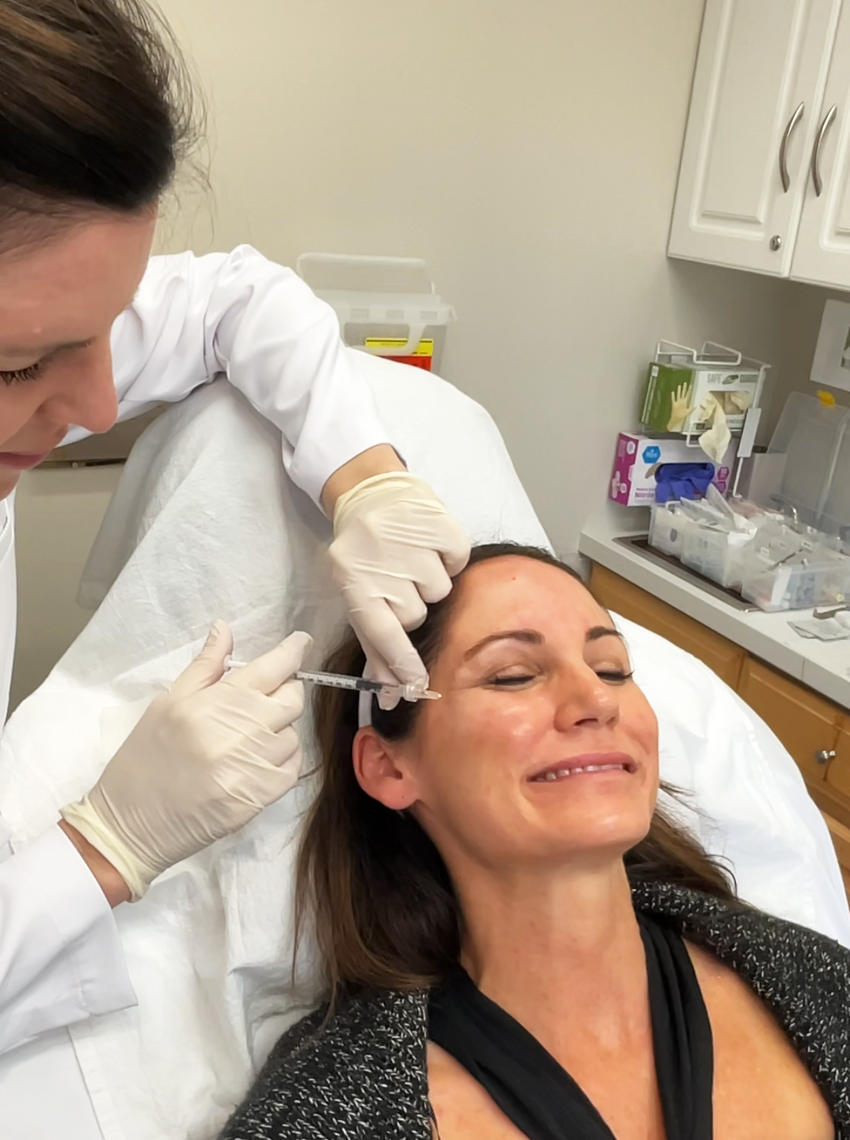 A woman receiving a cosmetic injection or Botox treatment on her forehead from a healthcare professional in a clinical setting.