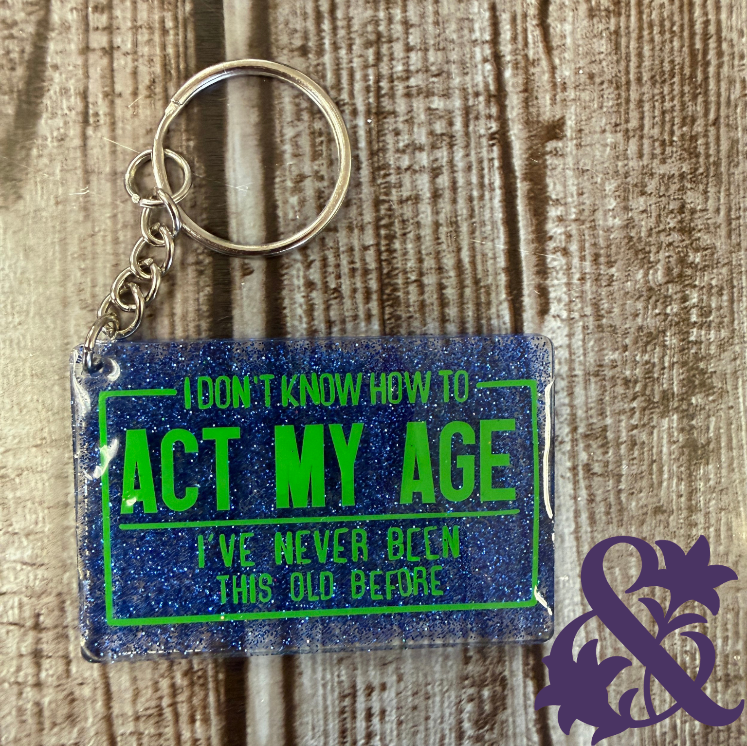 Blue glitter keychain reading, I don’t know how to act my age—I’ve never been this old before