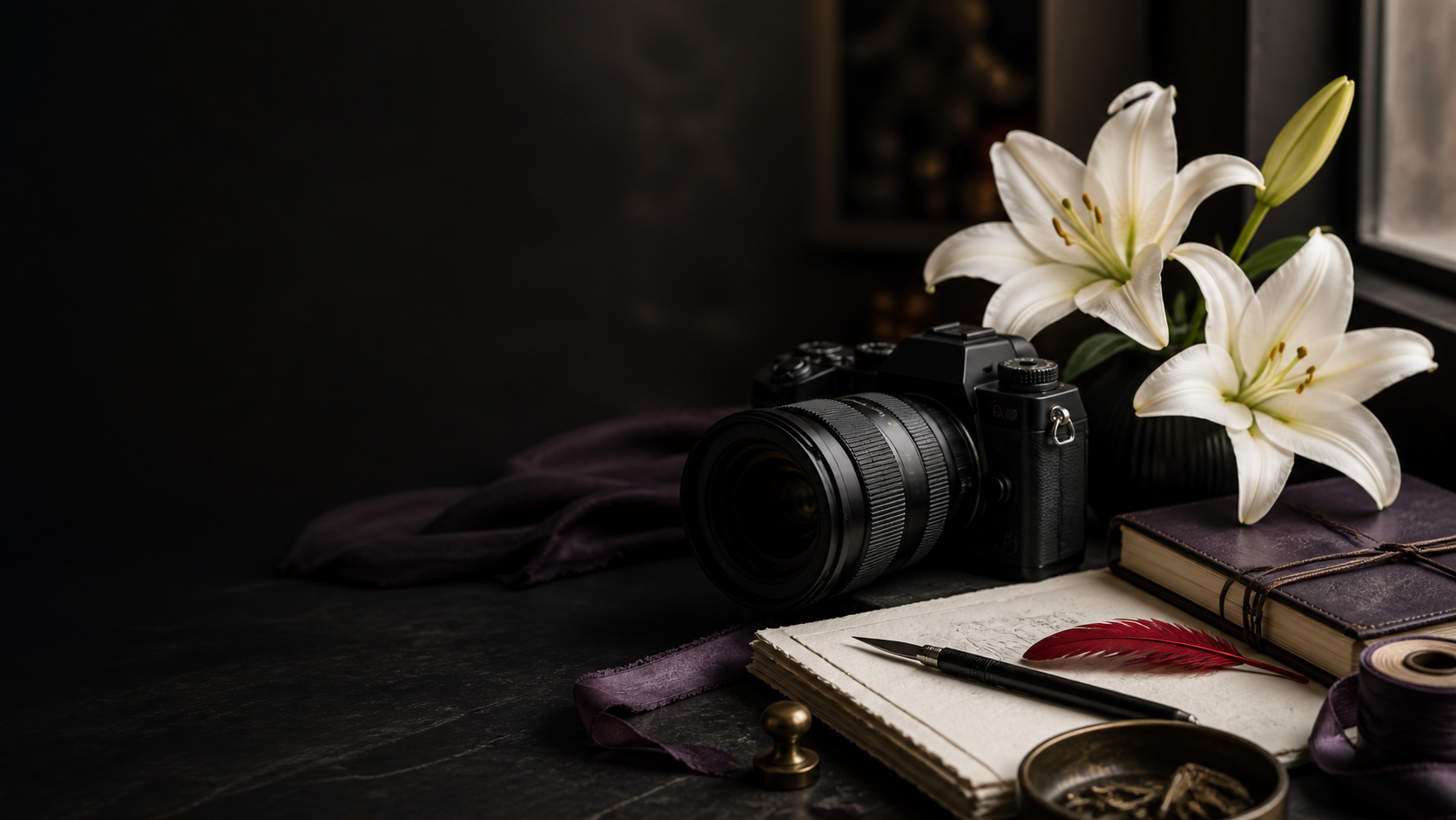 Black camera beside white lilies, a journal, writing paper, and a red feather on a dark creative workspace