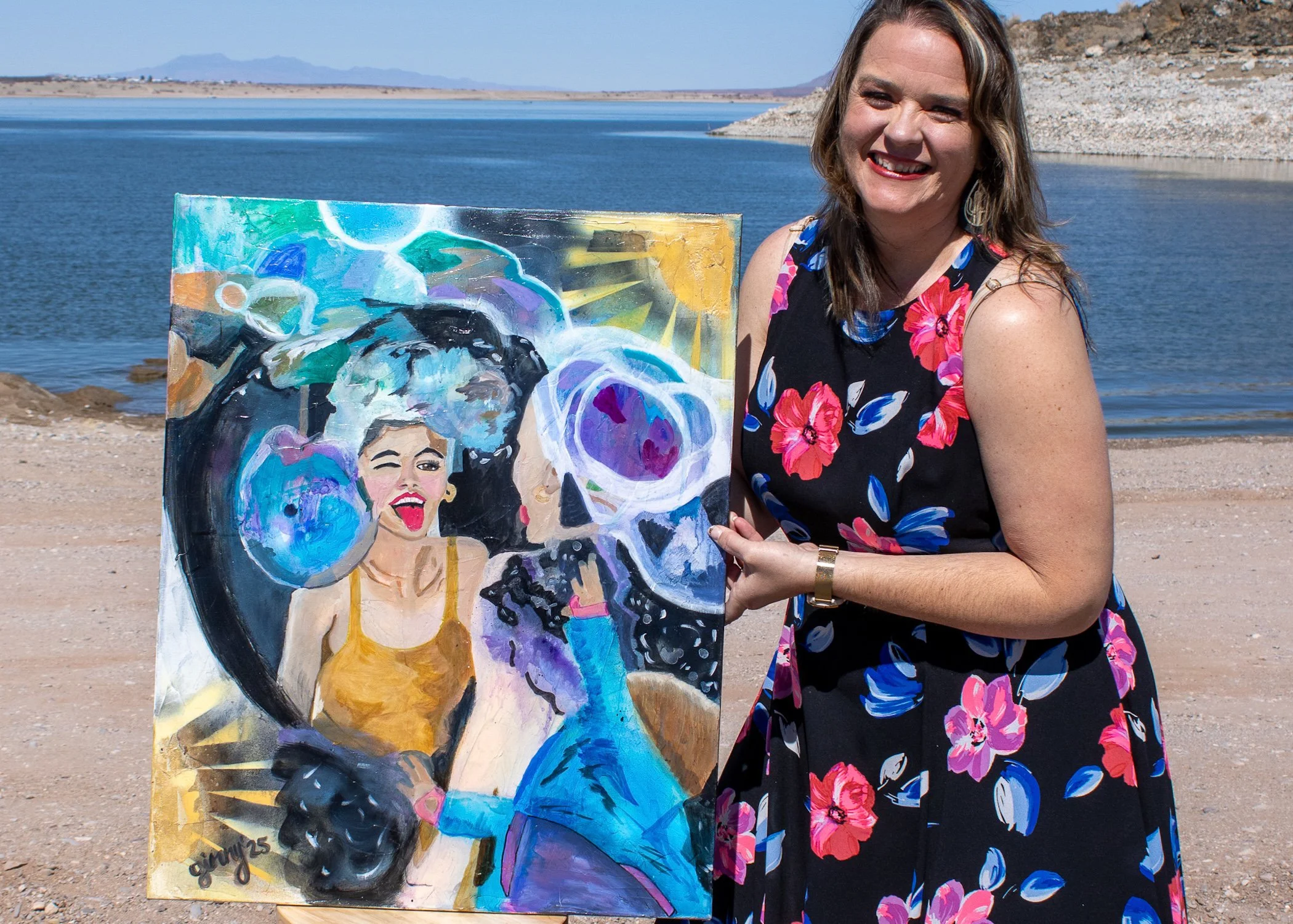 Smiling artist holding a colorful figurative painting beside a lake