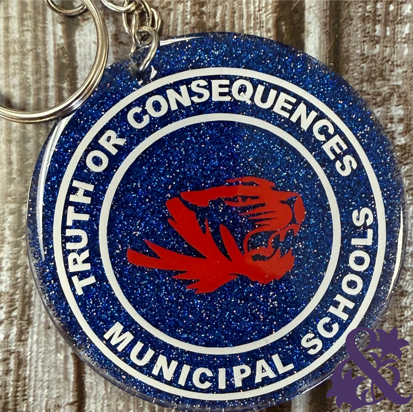 Round blue glitter Truth or Consequences Municipal Schools keychain with a red mascot design