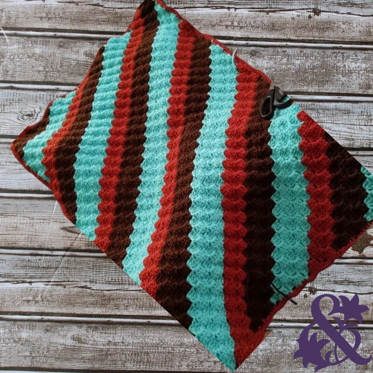 Handmade crocheted blanket with alternating teal, rust-red, and dark-brown textured stripes