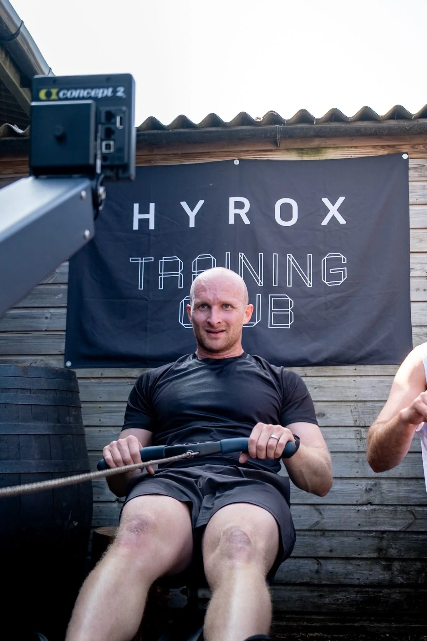 Man exercising at Hyrox training club, sitting on rowing machine outdoors