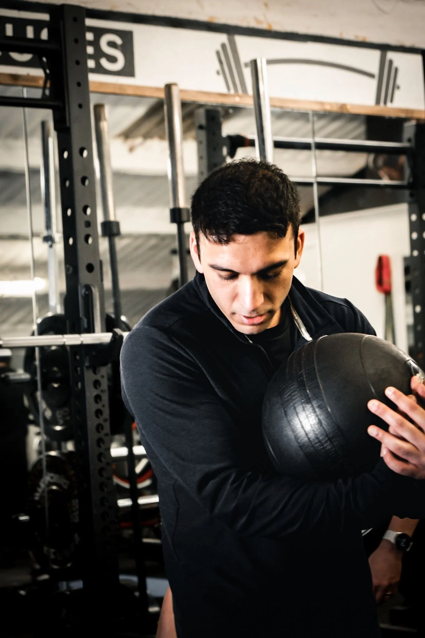 A young man in a gym holding a black medicine ball, preparing for exercise.
