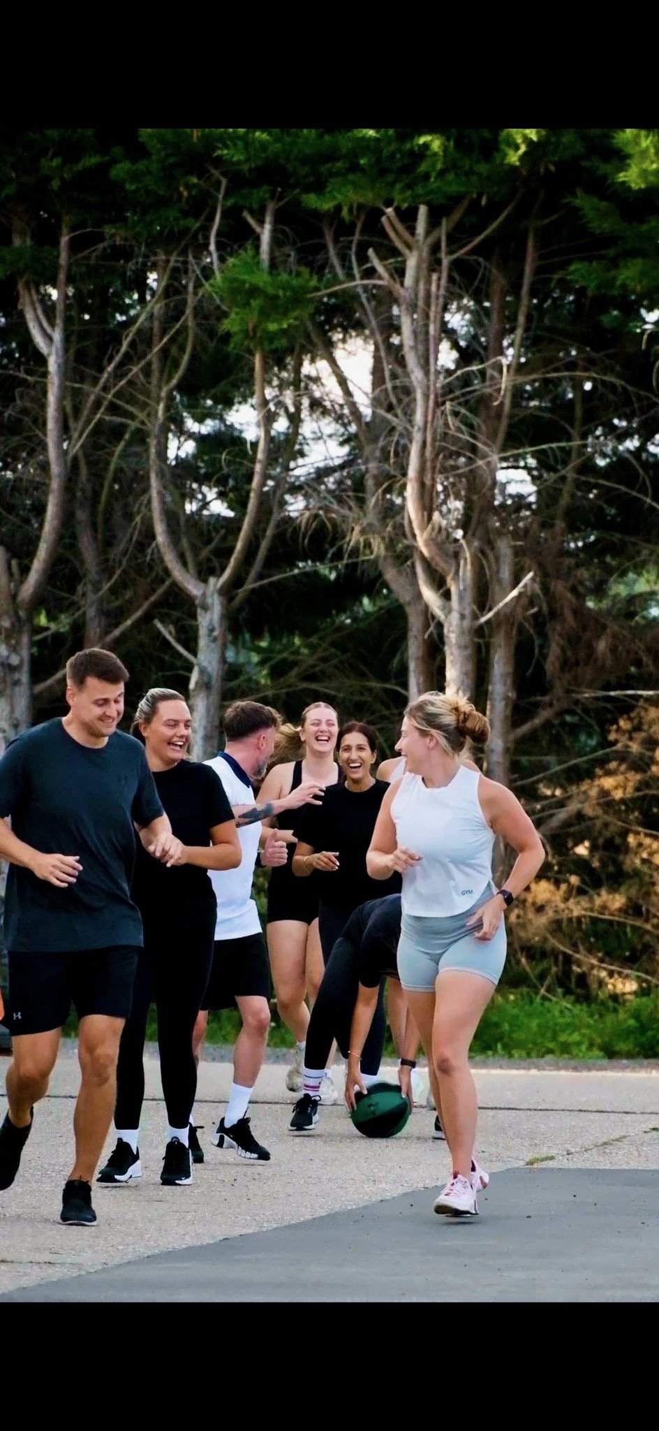 Group of people running outdoors, laughing and having fun, with trees in the background.