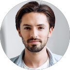 Headshot of a man with dark, styled hair and a beard, wearing a light-colored shirt.