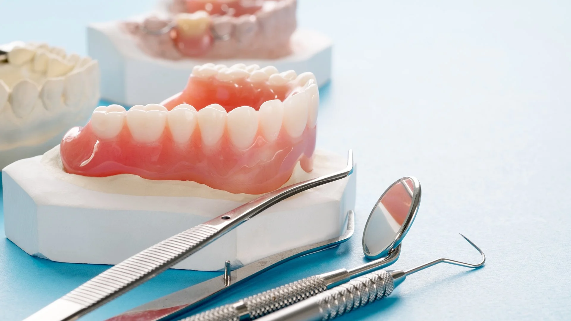 Set of dentures displayed on a dental model next to metal dental tools in a clinic setting