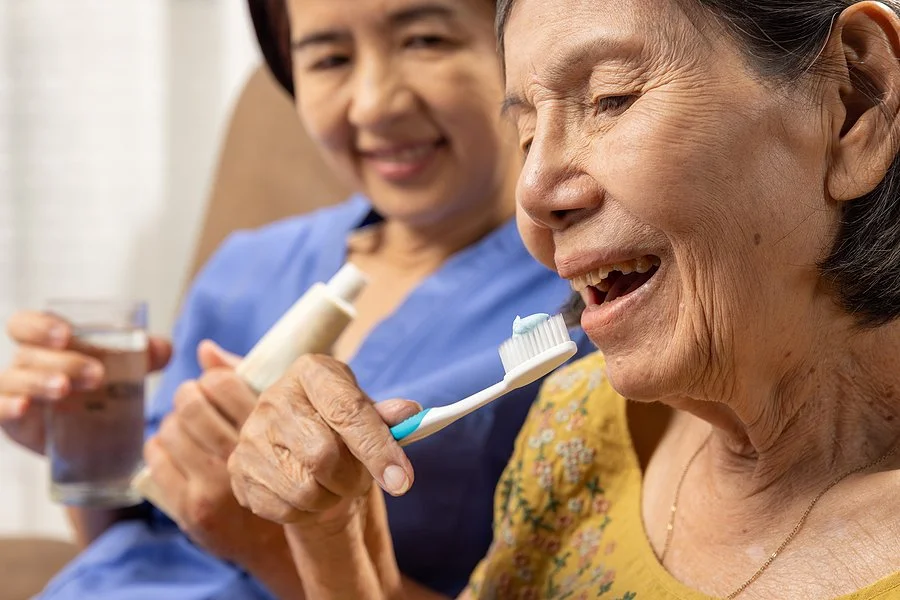 Older adult brushing teeth with assistance to demonstrate proper brushing techniques for better oral hygiene.