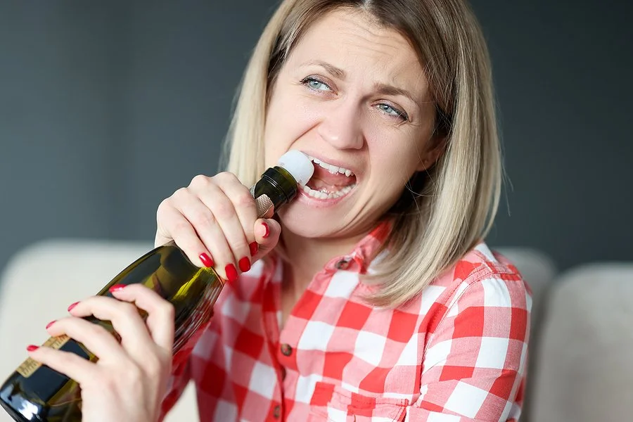Woman using her teeth to open a bottle, illustrating harmful oral habits that can damage teeth