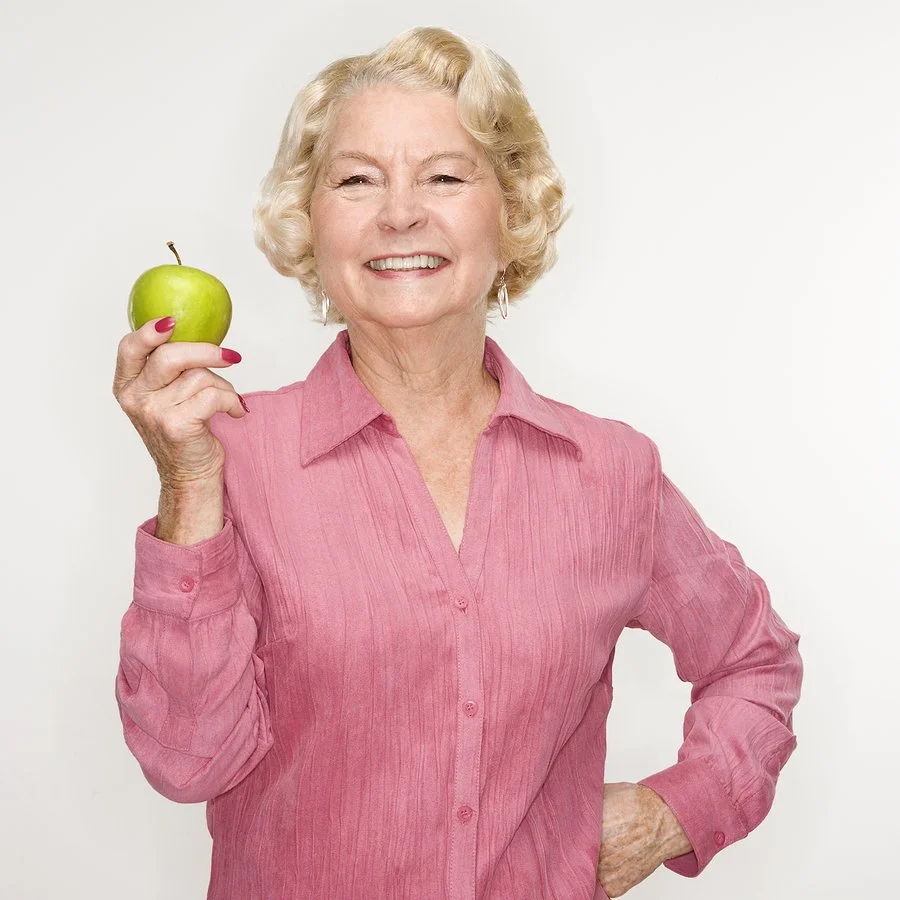 Older adult smiling confidently while holding an apple, illustrating the improved quality of life dental implants can provide for seniors