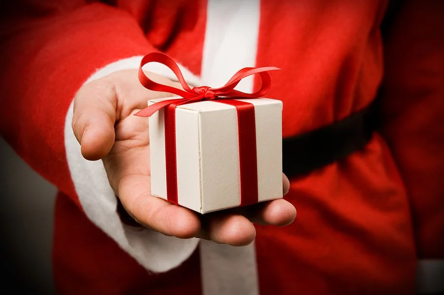 Hand holding a small wrapped gift to symbolize treating yourself to a brighter smile with veneers this Christmas