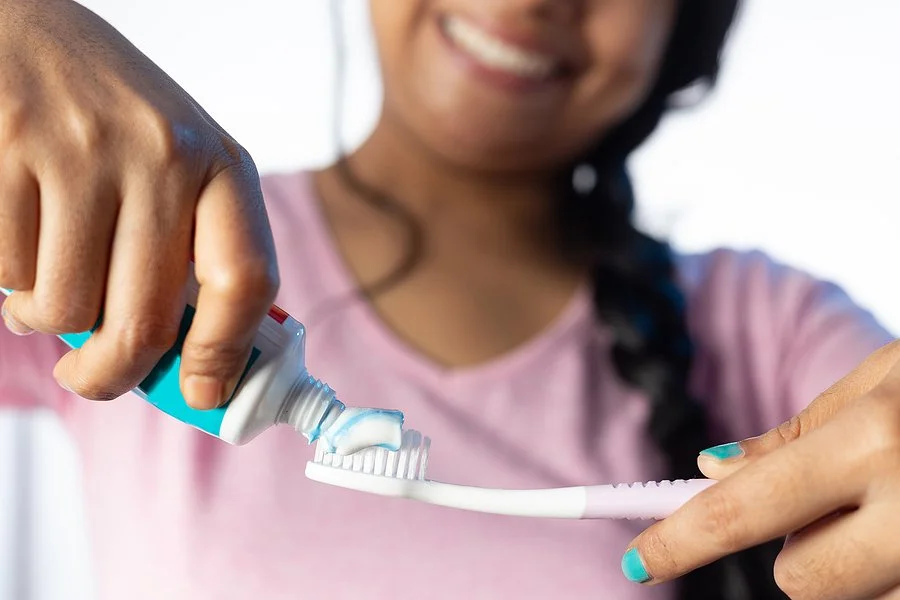 Person applying toothpaste to a toothbrush to highlight the importance of good dental hygiene while using Invisalign.