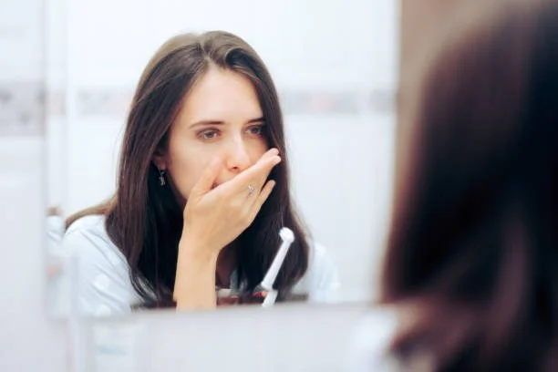 Woman covering her mouth while looking in the mirror due to bad breath concerns