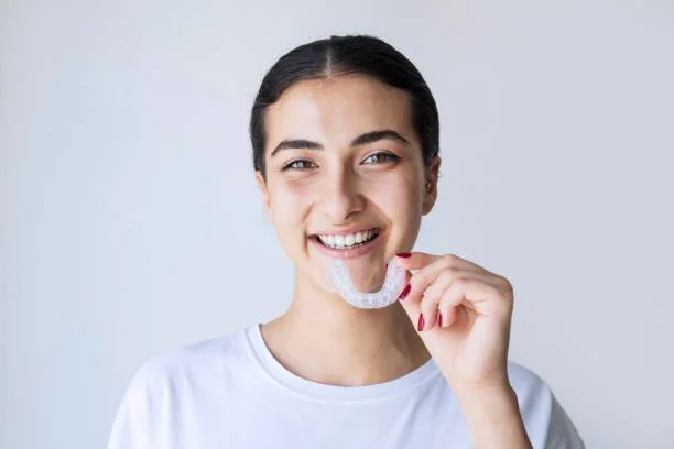 Person holding a clear night-guard in front of their mouth and smiling
