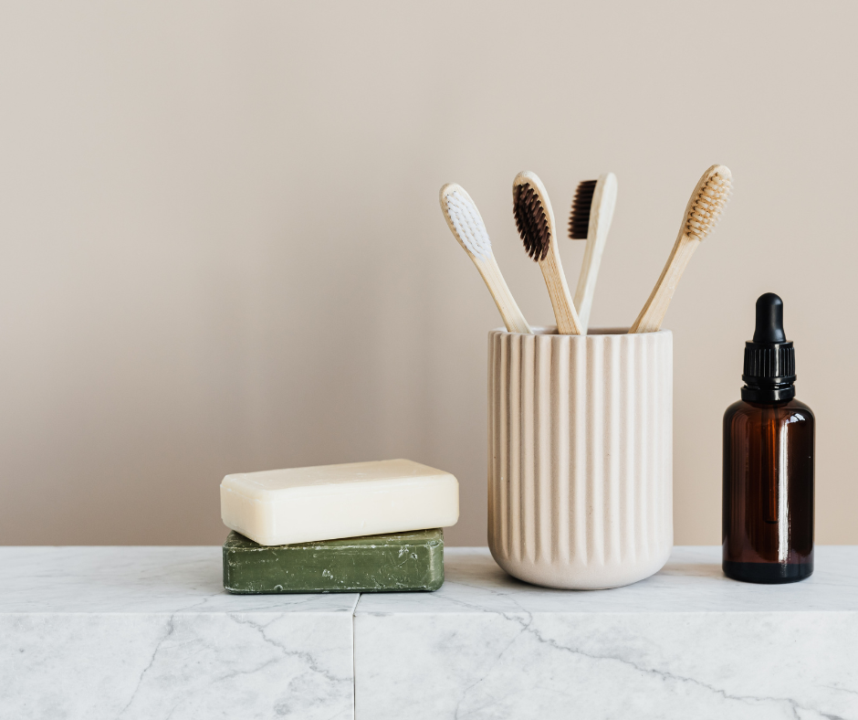 Eco-friendly toothbrushes in a ceramic cup with soap and hygiene items on a bathroom counter.