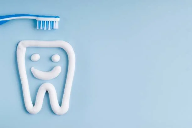 Toothpaste shaped like a smiling tooth next to a blue toothbrush on a light blue background