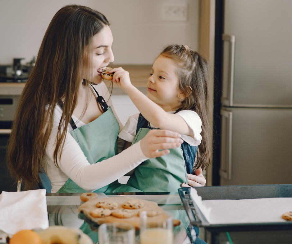 Mother and daughter baking together in the kitchen, with the child feeding her mom a treat, illustrating everyday use of xylitol-containing foods