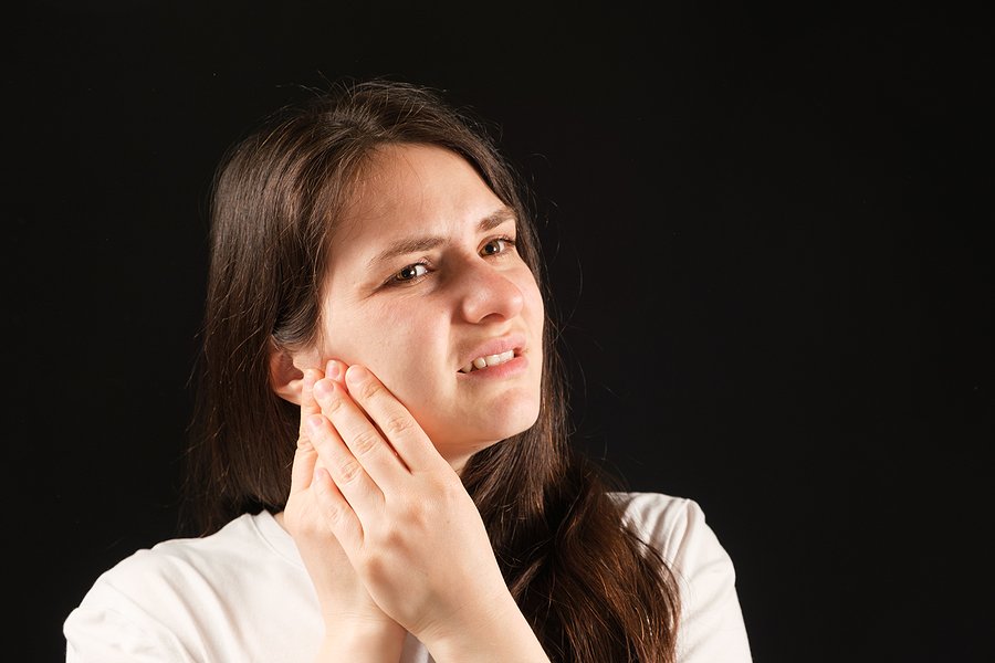 Woman holding her jaw in pain, illustrating symptoms of a dental emergency such as severe toothache