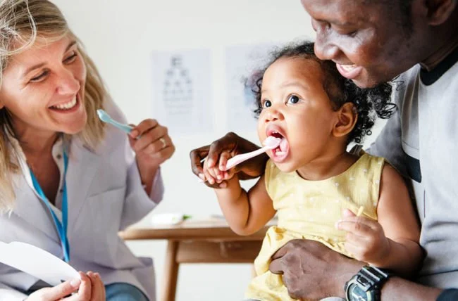 Dentist checking a young child’s mouth while a parent gently supports the child