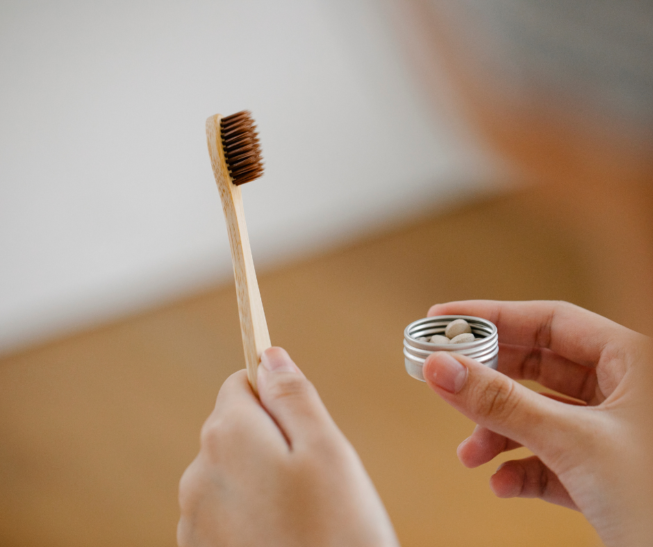 Person holding a bamboo toothbrush and a container of activated charcoal powder for natural teeth whitening