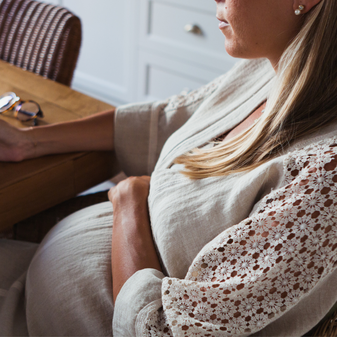 Pregnant woman sitting at a table with her hands on her belly, illustrating dental concerns during pregnancy