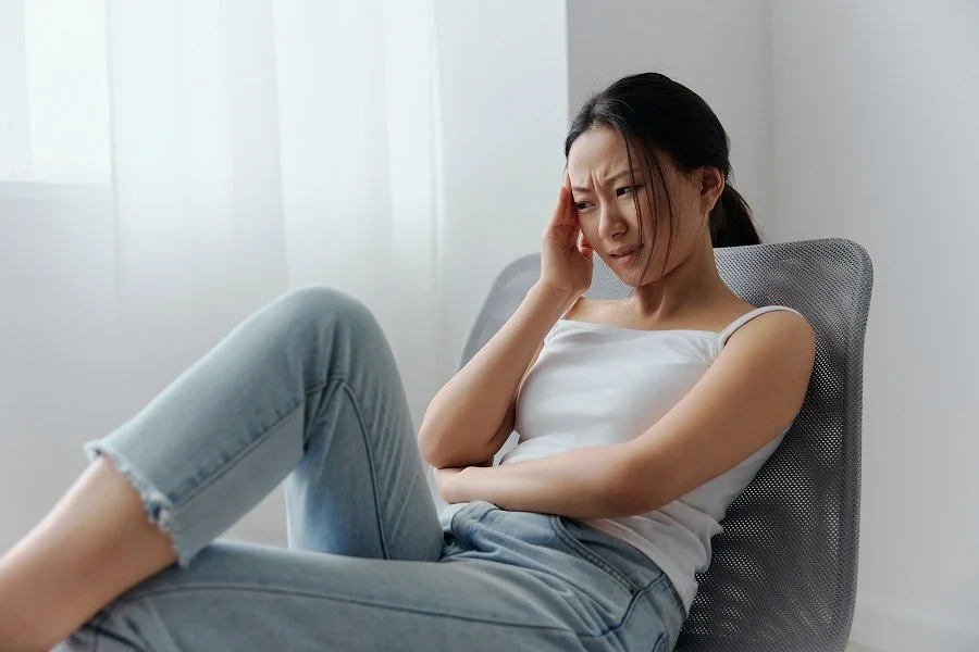 Woman sitting and holding her head in discomfort, representing how stress can lead to oral health issues