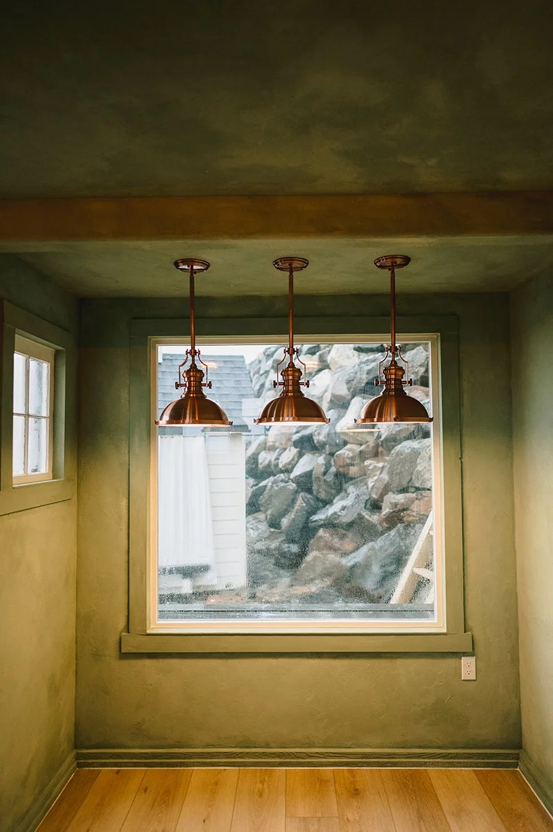 Warm glow of copper pendant lights against limewashed garden shed walls.